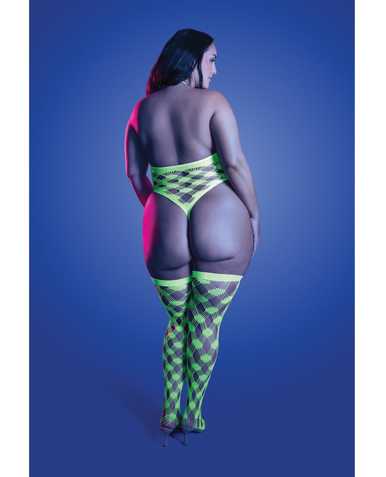 A plus-size model is shown from behind wearing a neon green and black harlequin-patterned thong and matching thigh-high stockings, set against a solid blue studio background.
