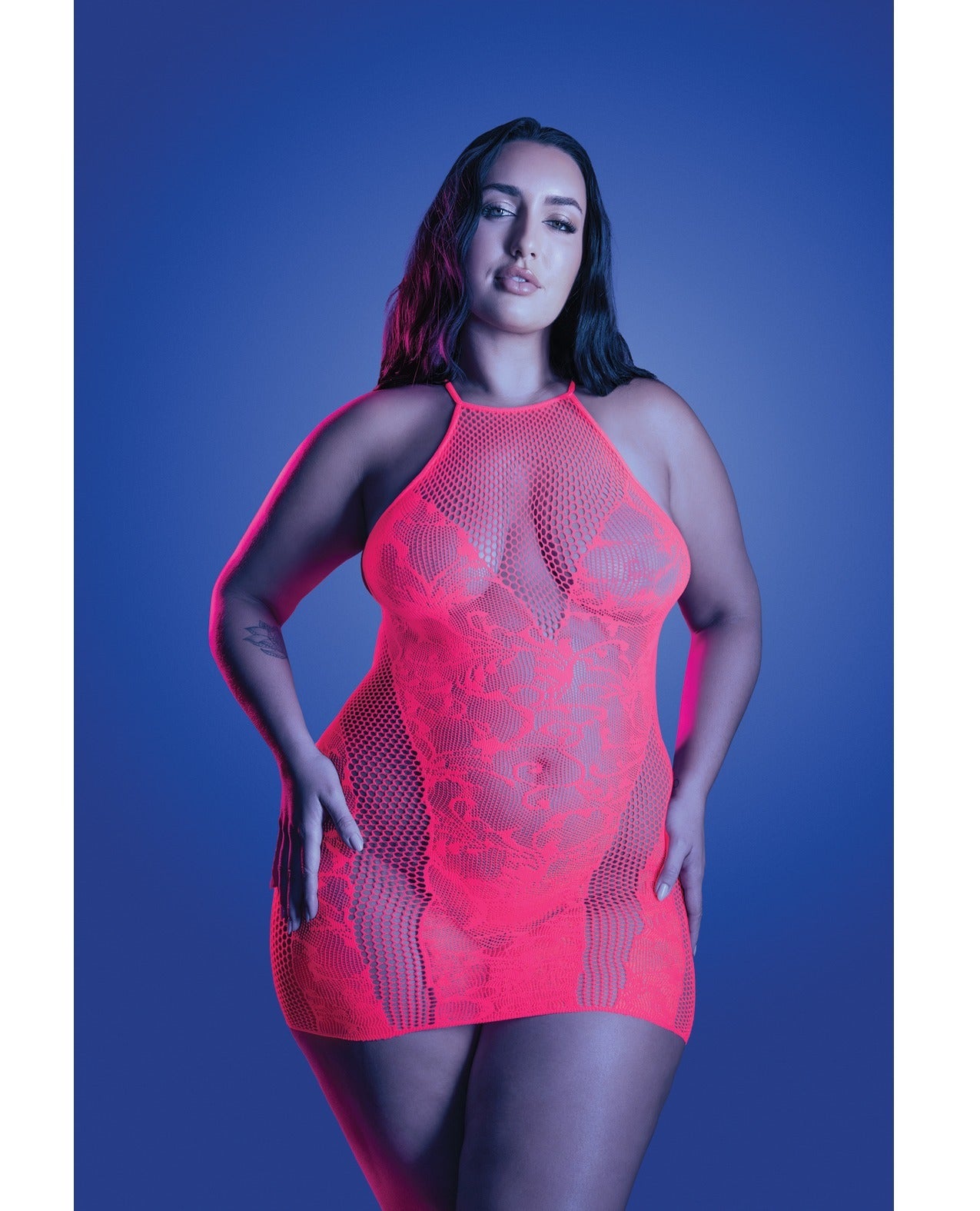 A woman modeling a bright neon pink fishnet halter bodysuit against a blue studio background.