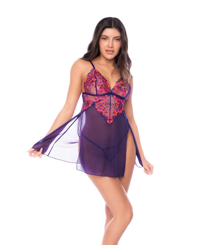 A woman modeling a sheer purple babydoll lingerie chemise with a floral lace bodice, set against a plain white background.