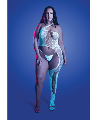A woman modeling a sheer, one-shoulder bodysuit and matching thong with integrated thigh-high stockings against a blue studio background.