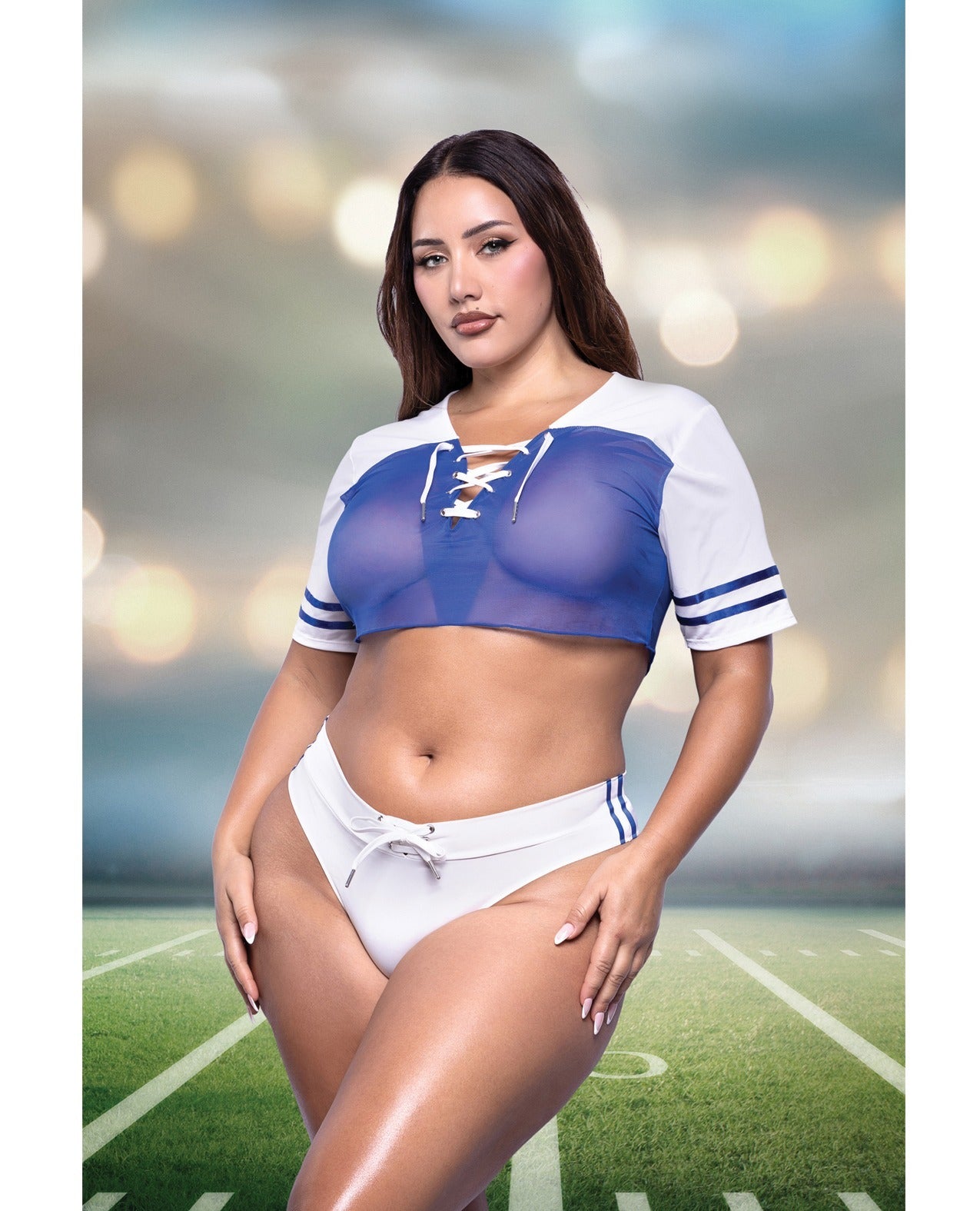 A woman modeling a two-piece athletic set consisting of a blue and white lace-up sports bra and matching white athletic bottoms with blue stripes, posed on a football field with a blurred stadium background.