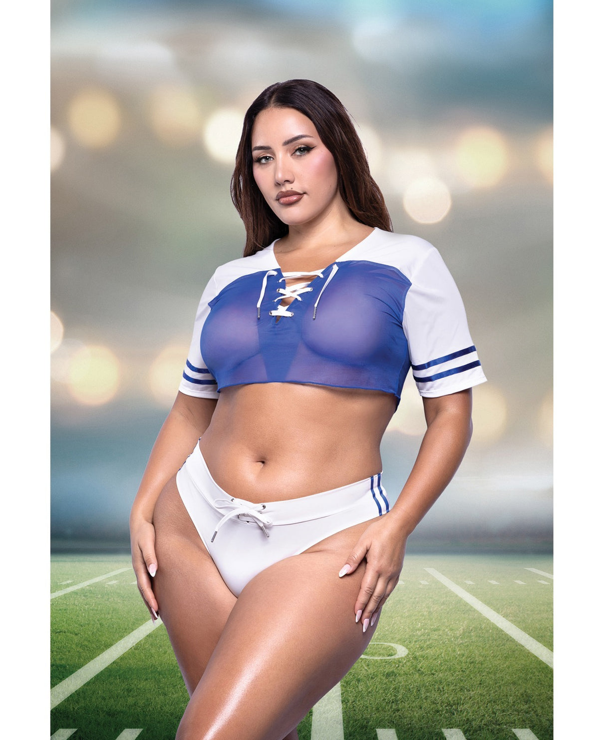 A woman modeling a two-piece athletic set consisting of a blue and white lace-up sports bra and matching white athletic bottoms with blue stripes, posed on a football field with a blurred stadium background.