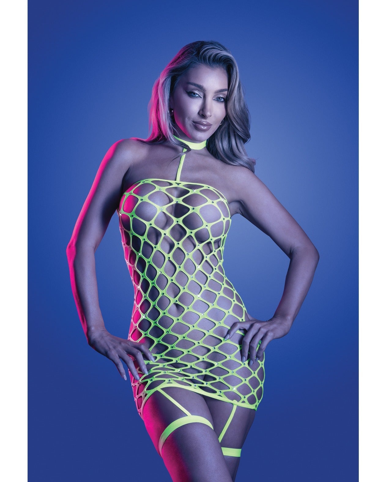 A model wearing a neon green fishnet halter mini dress with matching thigh straps, posed against a blue studio background with pink lighting.